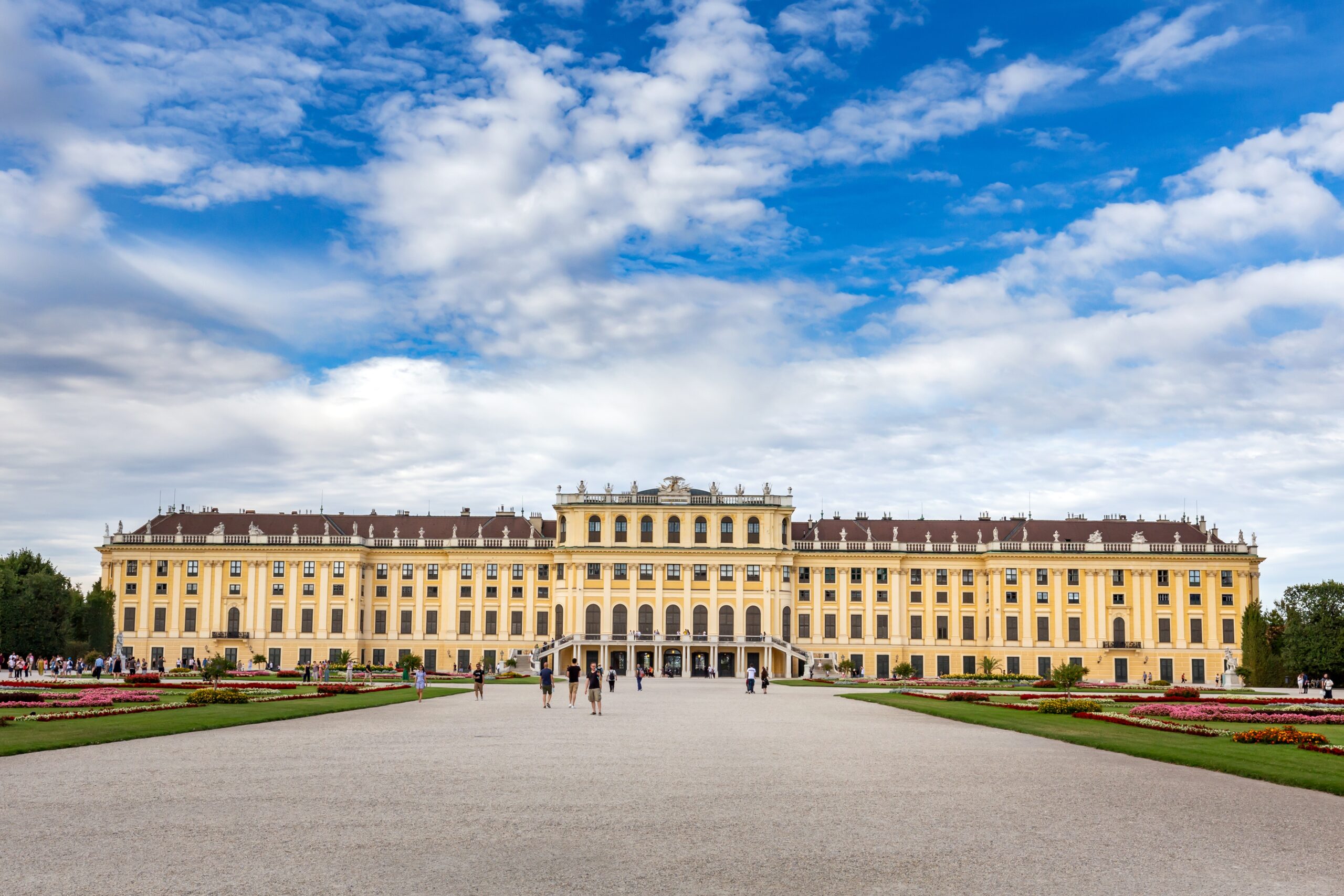 A wide-angle shot of schönbrunn palace in vienna, austria with a cloudy blue sky in the background